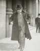Black and white photograph of James J. Hill walking down street with overcoat flapping, c.1915.
