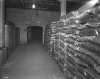 Black and white photograph of sacks of sugar produced by the American Crystal Sugar Company sit in a storage warehouse. Photographed by Norton & Peel on November 30, 1949