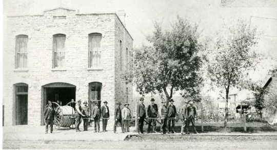 Black and white photograph of Cannon Falls firefighters posing in front of their headquarters. 