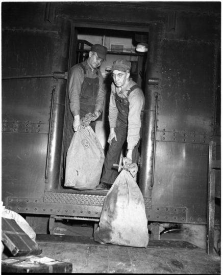 Railway Mail Service clerks load mail bags onto a Great Northern Railway Post Office car at the St. Paul Union Depot.