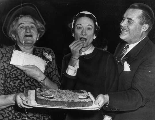 Black and white photograph of the Duchess of Windsor, the former Wallis Simpson, and Philip Pillsbury sample the grand prize winning orange kiss-me-cake cake, 1951.