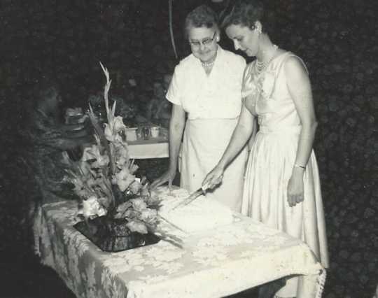 Black and white photograph of BPWC president Mary Louise Jorgenson (right) cuts cake for Ida Twedten (center), the first BPWC president, at a birthday party held for Twedten, 1966.