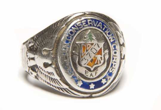 Color image of a Sterling silver Civilian Conservation Corps ring with CCC logo flanked by an eagle and shield on opposing ends. Logo is engraved with "3707/ and "EAF". Worn by Fred Fretheim of Company 3707, Two Harbors, MN, ca. 1936–1937. 