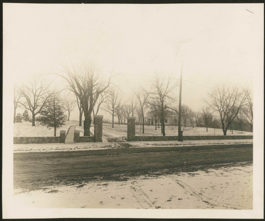 The stone fence added to the Woodbury House property by the Caswell family in 1911. Both the vehicle and pedestrian gates are visible, opening onto an unpaved Ferry Street. Photographer and exact date unknown. Anoka County Historical Society, Object ID# 2074.1.5. Used with the permission of Anoka County Historical Society.