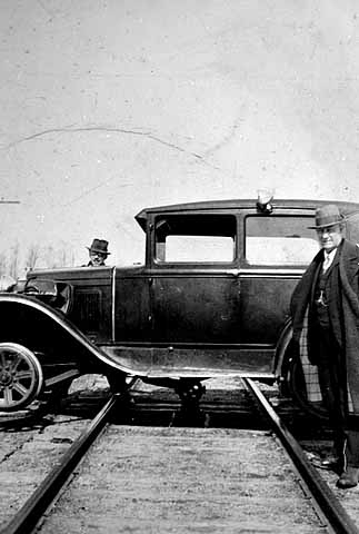 Photograph of a car straddling a railroad track. The car was used to transport Reverend John Sornberger to lumber camps c.1930.