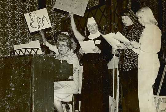 Black and white photograph of Sister Mary Magadalene, Marie Nelson (playing the piano), and other BPWC members sing a song promoting the Equal Rights Amendment, May 1977.