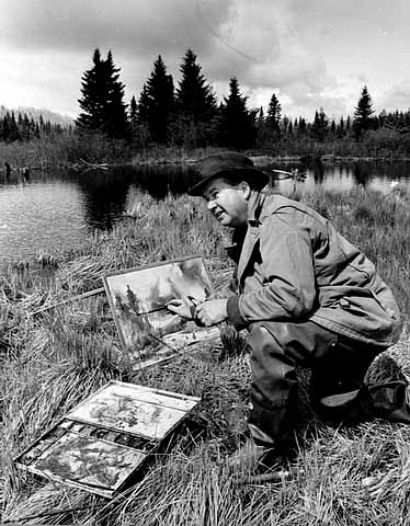 Birney Quick painting a landscape out in nature, along the shore of a lake, with pine trees in the background.