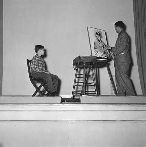 Black and white photograph of Birney Quick painting an image of a young man sitting on a chair in front of him.