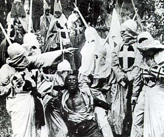 A scene from the movie Birth of a Nation (1915) featuring hooded Ku Klux Klan members surrounding Gus, a Black man portrayed in blackface by actor Walter Long. 
