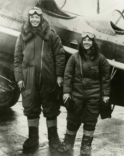 Black and white photograph of Charles and Anne Lindbergh in flight suits next to Lockheed Sirius during their flight across the Northern Pacific, c.1931.
