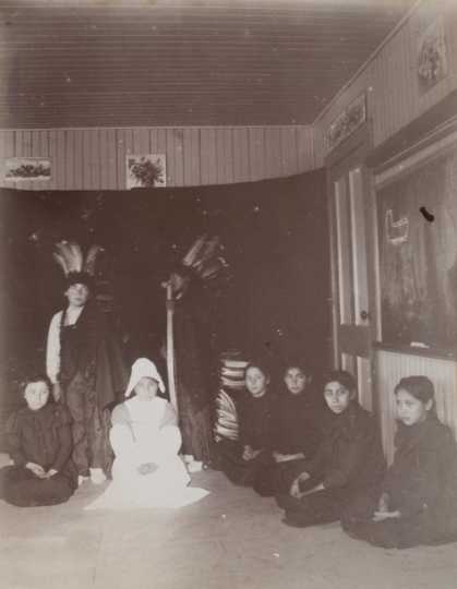 Black and white photograph of students at a Native American boarding school perform a Thanksgiving play, c.1900.