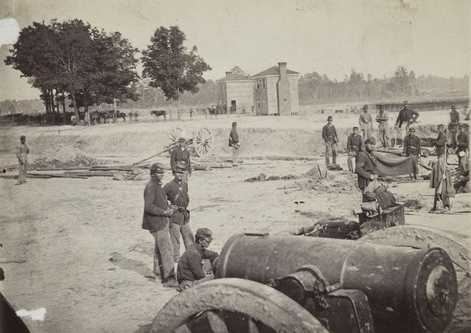 Black and white photograph of men of the First Minnesota Volunteer Infantry in field works after the battlefield of Fair Oaks, Virginia, 1862. Evidence of the newly-attached Company L, the Second Company Minnesota of Sharpshooters, can be seen in the center-right of the photograph: a Sharps breech-loading rifle is hanging over a blanket.
