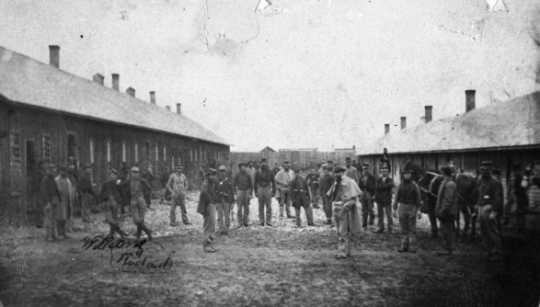 Black and white photograph of some members of the First Minnesota Mounted Rangers in front of temporary barracks outside the walls of Fort Snelling, 1864.