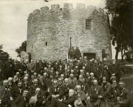 Black and white photograph of a reunion of First Minnesota Volunteer Infantry Regiment, posed in front of Round Tower, 1902.