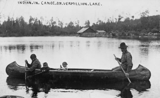 Black and white photograph of an Ojibwe family in canoe on Lake Vermilion, ca. 1905. 