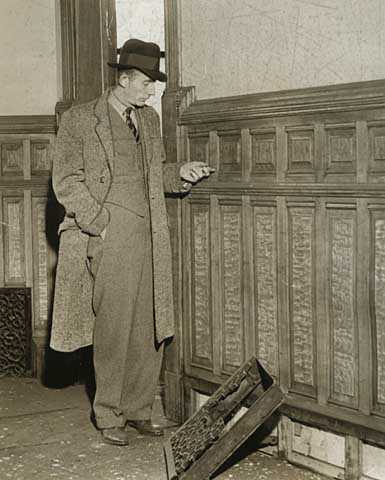 Black and white photograph of Richard R. Sackett, in charge of a historical records survey crew salvaging old documents at the second state capitol prior to demolition, inspects oak paneling, 1937. Photographed by the Minneapolis Tribune.