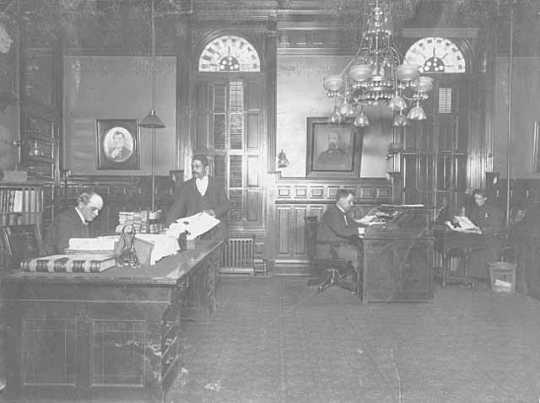 Minnesota governor's suite during John Lind's administration, c.1900. Pictured: John Lind at his desk; G. P. Wade, postmaster of the Legislature; L. A. Rosing, private secretary to the governor; and an unidentified woman.