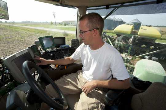 Color image of a farm worker adjusting GPS equipment inside the cab of a planter, June 25, 2009. Used courtesy of the United Soybean Board.