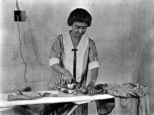 Black and white photograph of a woman on a farm ironing, ca. 1925.