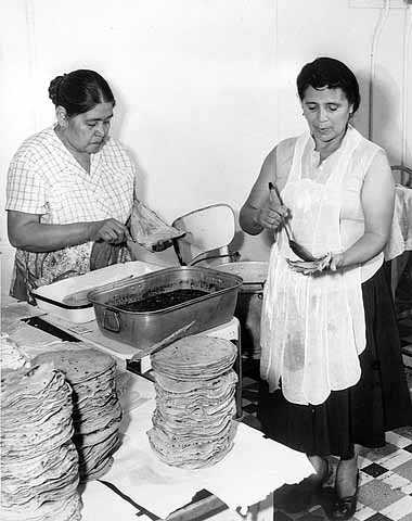 Black and white photograph of Mrs. Julio Lopez and Mrs. Francisco Rangle prepare food for an Mexican Independence celebration, Our Lady of Guadaloupe Church, September 15, 1958.