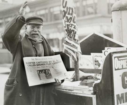 Black and white photograph of a man selling a newspaper with headline related to Bremer kidnapping, 1935. 