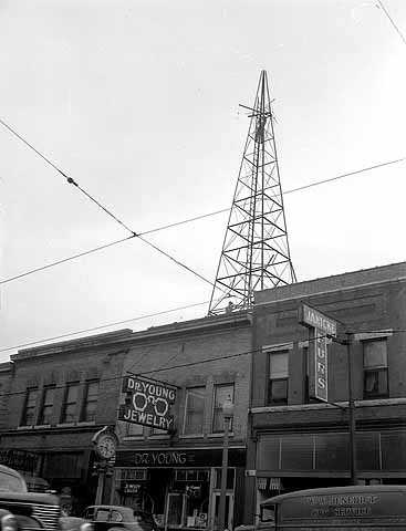 Black and white photograph of a WDGY radio tower, 1947. Photographed by the Minneapolis Star Journal.  The optometry shop of Dr. George Young, the founder of WDGY, is visible below the tower.