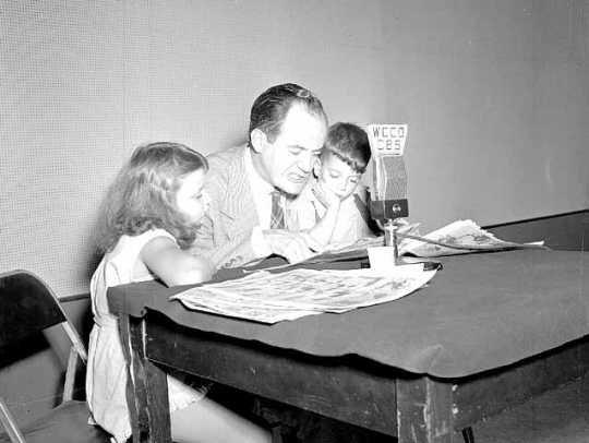 Black and white photograph of Hubert Humphrey reading comics on the radio, August 1946.