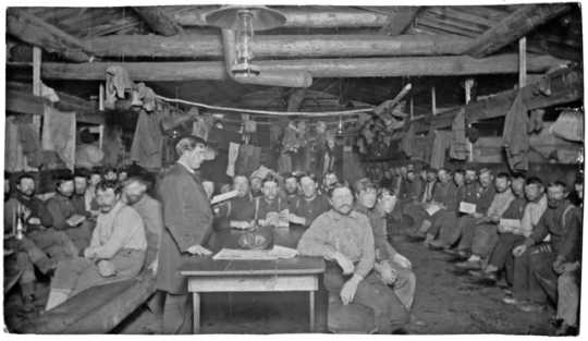 Photograph of Frank Higgins preaching to a group of lumberjacks in a bunkhouse c.1910.