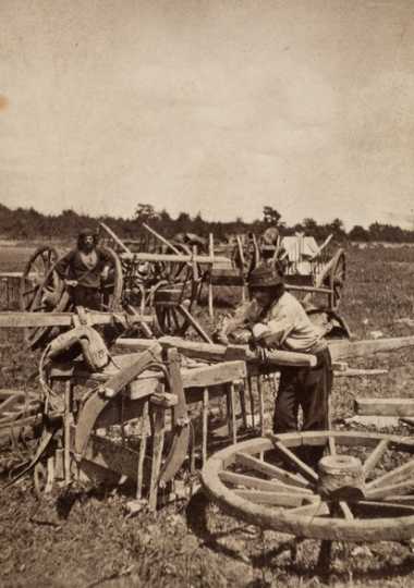 Black and white photograph of two men, probably Métis, preparing a Red River cart train at Pembina, 1856. 