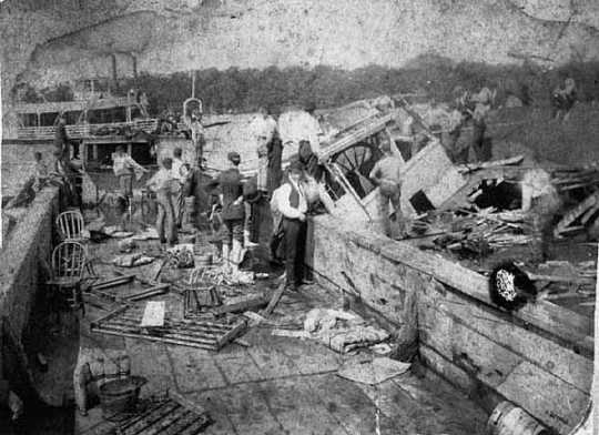 Black and white photograph of National Guardsmen searching for survivors in the wreckage of the Sea Wing, 1890. The men at left are standing in the Sea Wing’s attached barge, Jim Grant. The Lake City steamer Ethel Howard is in the background.