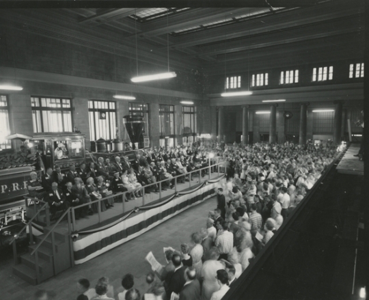 Black and white photograph of speaker’s stand and crowd at the 100th anniversary celebration of the Great Northern Railway at St. Paul’s Union Depot, 1962. 