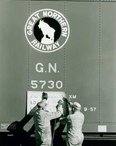 Black and white photograph of load capacity figures being stenciled on a Great Northern Railway boxcar, ca. 1957.