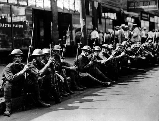 Black and white photograph of the National Guard seated along street curb, Minneapolis, 1934.