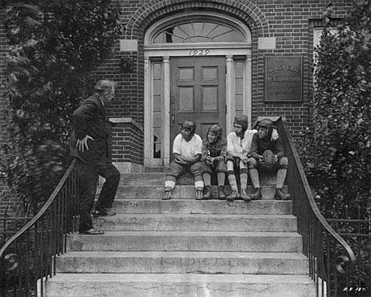 Black and white photograph of a boys wearing football helmets on the front steps of the Northeast Neighborhood House, 1927.