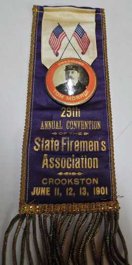 Color image of a badge worn by Fire Chief Tom Morris at the Firemen’s Convention held at Crookston city hall, 1901.