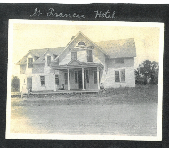 Photograph of the front of the Riverside Hotel, sometimes called the St. Francis Hotel. Four people stand or sit on the porch. Anoka County Historical Society, Object ID# JE0038-2. Used with the permission of Anoka County Historical Society.