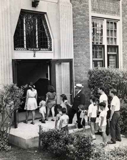 Black and white photograph of adults and children walk through the entrance of the J. E. C., c.1940.