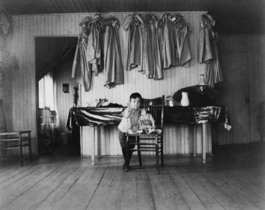 Black and white photograph of a young child inside a Native American boarding school, c.1890s.