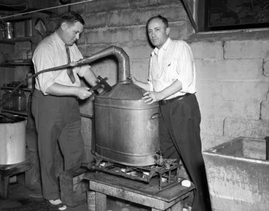 Black and white photograph of two men breaking apart an illegal still,1940. Photographed by the Minneapolis Star Tribune.
