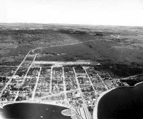 An aerial view of Grand Marais, ca. 1955. The diagonal white line that can be seen in the background is the Gunflint Trail.