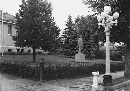 Black and white photograph of the statue of Leonidas Merritt in front of the public library in the town of Mountain Iron, 1940.