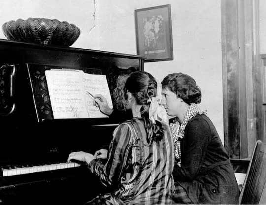 Black and white photograph of a girl being given piano lesson at the Northeast Neighborhood House, c.1925.