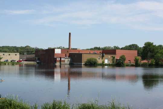 Color image of north and west façades of Faribault Woolen Mill with Cannon River in the foreground, 2011.
