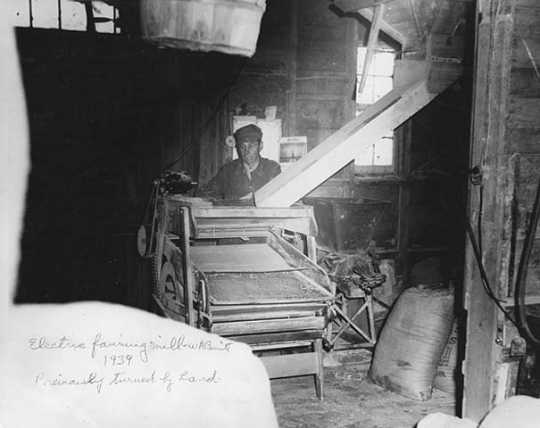 Black and white photograph of a man operating electric fanning mill, W. A. Benitt farm, Dakota County, 1939.