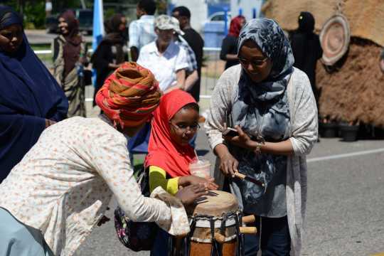 Photograph of a child playing a traditional Somali drum with help from adults