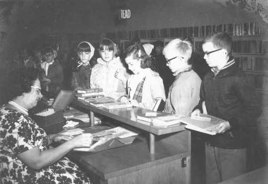 Photograph shows children waiting to check out books at the Waconia Public Library