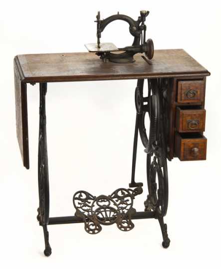 Noiseless Automatic Sewing Machine designed by by the Willcox & Gibbs Sewing Machine Company in London, England. The treadle and gears run smoothly on this chain stitch sewing machine. The machine is mounted on a wooden table with an iron base, a foot treadle, and three drawers.