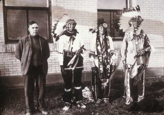 Black and white photograph of a translator with three Ojibwe men. The Ojibwe leader Miskogwan (Red Feather) stands on the far right. Northwest School of Agriculture Dedication Day, October 5, 1920.