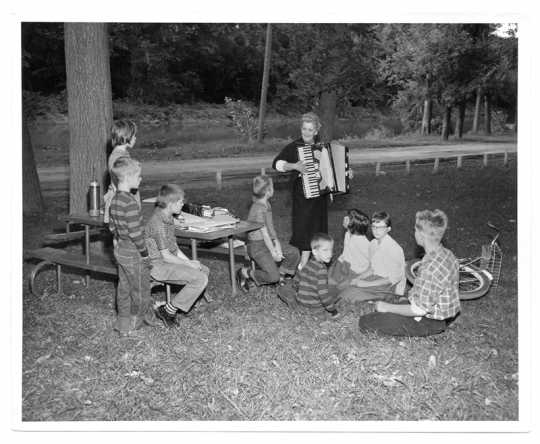 Knutson playing her accordion for a group of children in a park